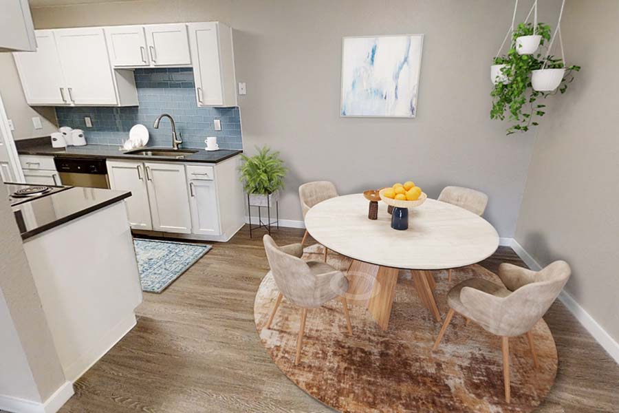 Fully furnished apartment dining room and kitchen area with table, chairs, white cabinetry.